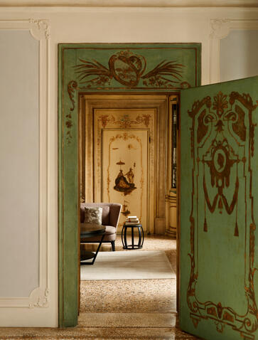 Alcova Tiepolo suite living room at Aman Venice, with green-painted doors opening to reveal period furnishings and classical décor.
