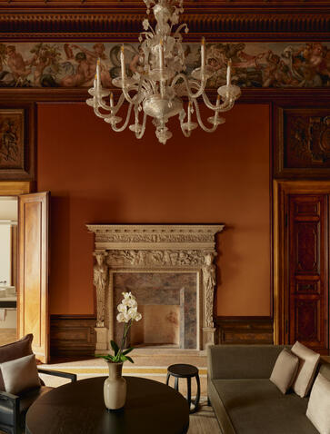 Sansovino Stanza bedroom at Aman Venice with ornate fireplace, crystal chandelier, and period furnishings.