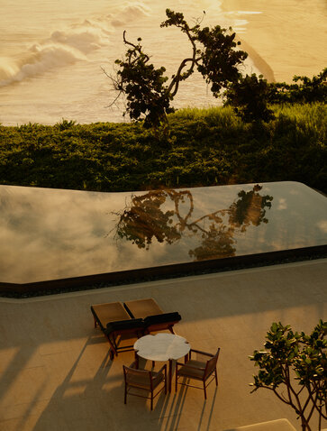 Wooden dining table and chairs positioned on a terrace overlooking the main pool at Amanera, Dominican Republic, at sunset.