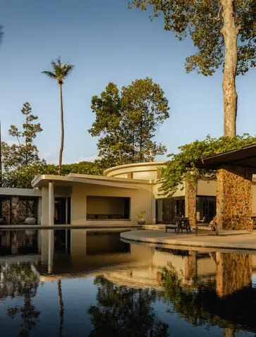Amansara pavilion reflected in still water, surrounded by tropical trees at dawn.