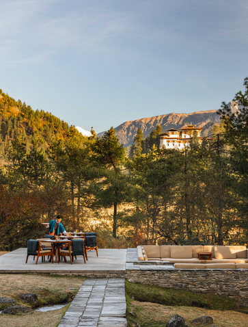 Amankora Paro Lodge nestled among forested mountains in Bhutan's Paro Valley at golden hour.