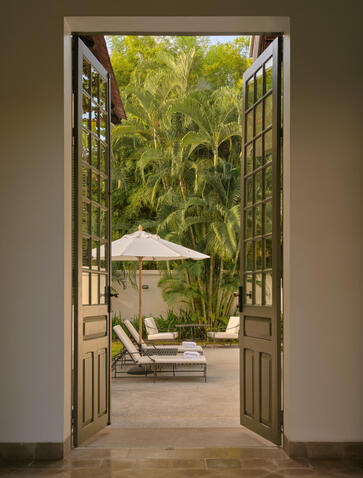 Khan Pool Suite outdoor terrace at Amantaka, looking through open doors to poolside seating and lush gardens.