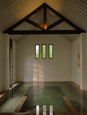 Sunlit Laotian bathing house at Amantaka with wooden beam ceiling and reflecting pool.