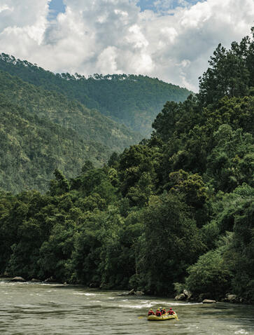 Whitewater rafting on a river surrounded by forested mountains at Aman Bhutan.