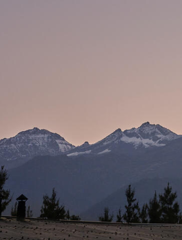 Amankora Bhutan Paro Lodge mountain view at dusk, snow-capped peaks rising above forested slopes.