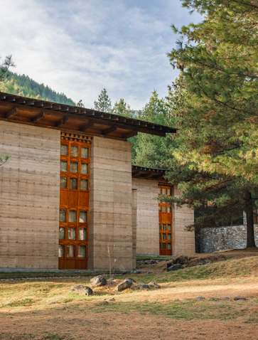 Amankora Paro Lodge exterior with stone and timber architecture nestled among Bhutanese forest.