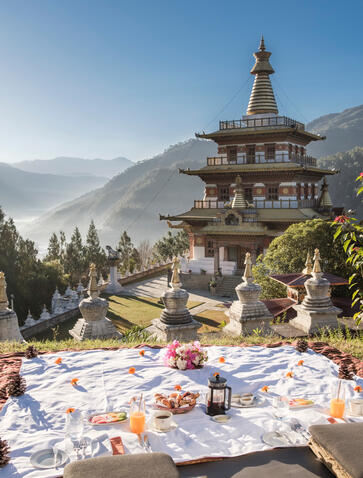 Breakfast spread laid out on white tablecloths at Aman Bhutan in Punakha, with the golden Khamsun Chorten temple visible on the hillside beyond.