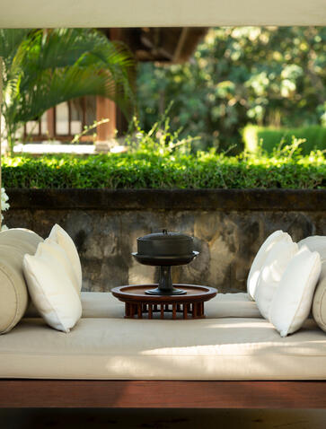 Outdoor seating area at Aman Villas at Nusa Dua with white cushioned bench and lush greenery.