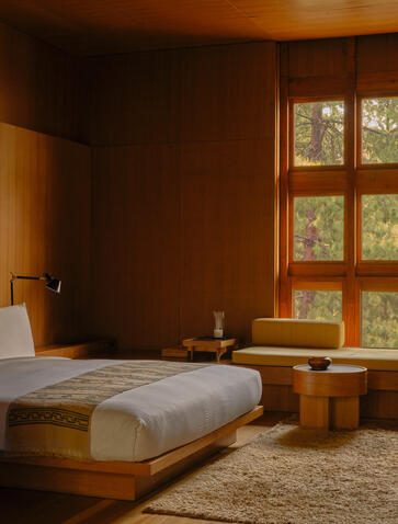 Principal bedroom suite at Amankora's Paro Lodge with warm wood panelling and mountain views through glazed windows.