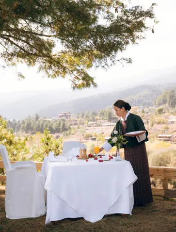 Staff member arranging lunch table at Amankora Bumthang Lodge with monastery views across the valley.