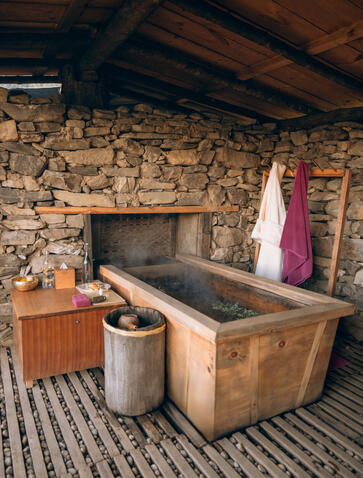 Traditional hot stone bath at Gangtey Lodge, Amankora, with wooden tub and stone fireplace.
