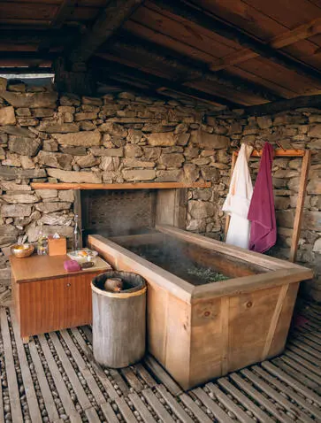 Traditional hot stone bath at Gangtey Lodge, Amankora, with wooden tub and stone fireplace.