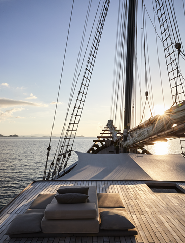 Wooden deck of sailing vessel at Amandira with rigging and sails visible at sundown, overlooking calm waters.
