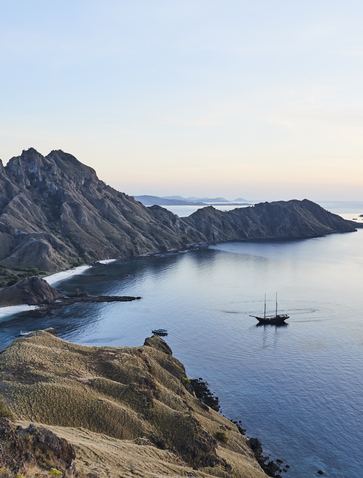 Sailboat anchored in calm waters off Pulau Padar, Indonesia, with volcanic peaks rising above the shoreline at Amandira.