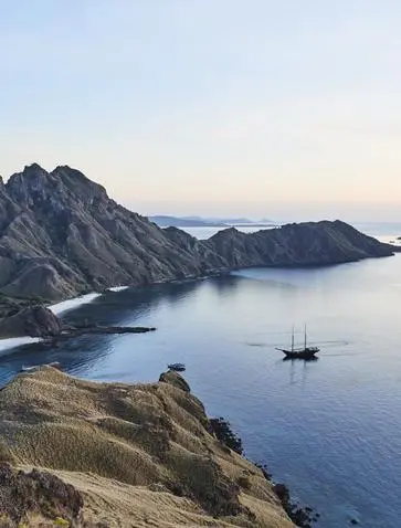 Sailboat anchored in calm waters off Pulau Padar, Indonesia, with volcanic peaks rising above the shoreline at Amandira.