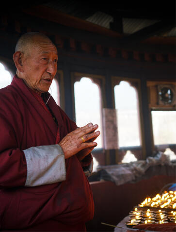 Buddhist monk in maroon robes lighting butter lamps during ceremony at Kyichu Lhakhang, Amankora, Bhutan.
