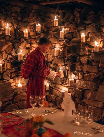 Monk in burgundy robes standing among candlelit offerings at Amankora's Gangtey Lodge potato shed dinner.