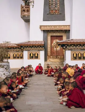 Monks in crimson robes seated on the ground receiving a meal offering at Amankora, Gangtey, Bhutan.