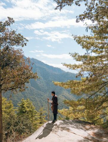 Hiker standing on mountain path overlooking forested valley at Amankora's Paro Lodge, Tigers Nest trek.