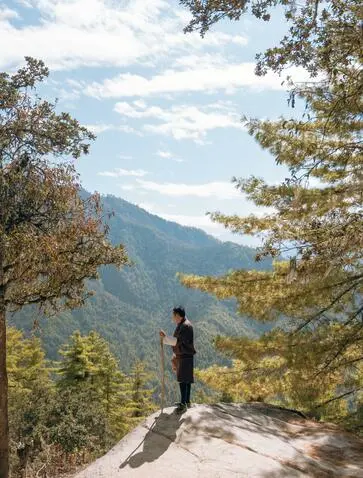 Hiker standing on mountain path overlooking forested valley at Amankora's Paro Lodge, Tigers Nest trek.