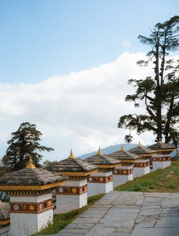 Amankora in Punakha with traditional Bhutanese architecture and prayer flags along a stone pathway, mountains in the distance.