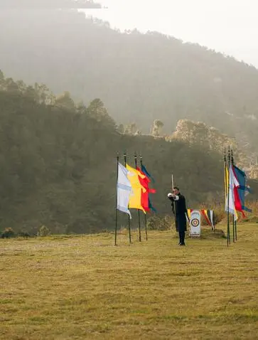 Archer practising traditional Bhutanese archery at Amankora in Punakha, with national flags and misty mountains beyond.