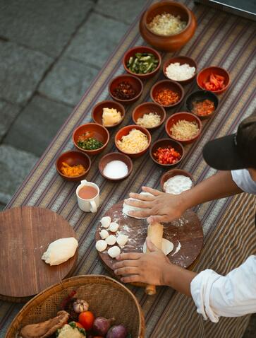 Overhead view of a Bhutanese cooking class at Amankora, with small bowls of spices and ingredients arranged on a wooden surface, a hand reaching for a glass of water.