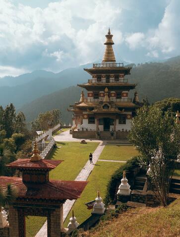 Khamsum Chorten, a golden-roofed Buddhist temple, rises above manicured gardens with Bhutanese mountains in the distance at Amankora.
