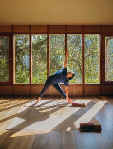 A guest practises yoga in a sunlit studio at Amankora, Bhutan, with windows overlooking the landscape.