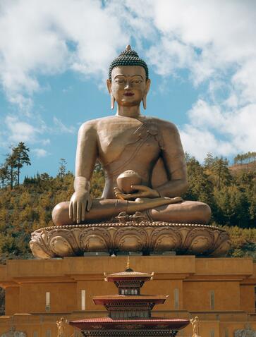 Golden Buddha statue at Amankora in Thimphu, Bhutan, seated against cloudy sky.