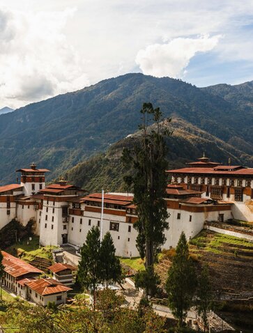 Trongsa Dzong fortress perched on a mountainside at Amankora, Bhutan, with forested peaks beyond.