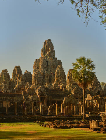 Golden light illuminates the ancient stone towers of Bayon temple at Amansara, with palm trees framing the architectural spires.