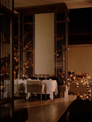 Evening view of an intimate dining space at Aman Nai Lert Bangkok, candlelit and decorated with warm string lights.