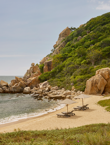 Amanoi's private beach with sandy shore, rocky outcrops and sun loungers facing turquoise waters.