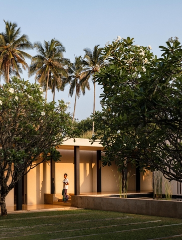 Amanwella architecture detail showing a contemporary pavilion with warm-toned walls framed by tropical palms at dusk, Sri Lanka.