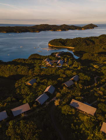 Amanemu resort viewed from above at dusk, with coastal landscape and illuminated outdoor spaces nestled along the Japanese shoreline.