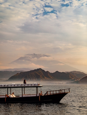 Wooden boat on calm water at sunrise, with Mount Agung visible across the bay at Amankila, Bali.