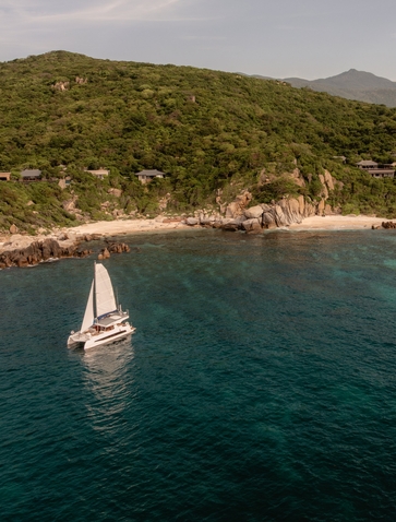 Aerial view of a catamaran sailing off the forested coastline at Amanoi, Vietnam.