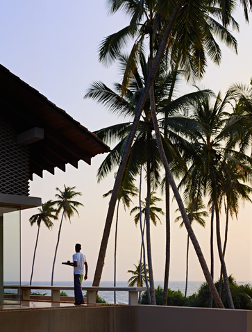 Amanwella's exterior at dusk with palm trees and a figure standing on the terrace.