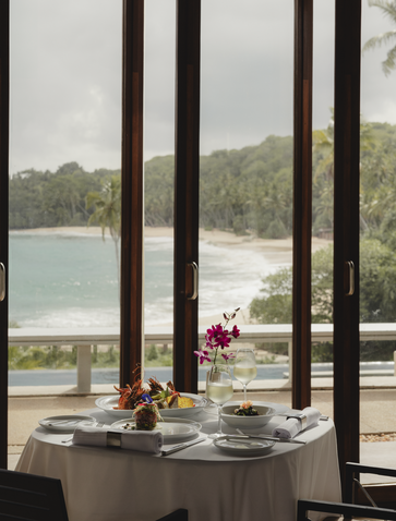 Dining table at Amanwella with views across the lagoon framed by tall wooden columns.