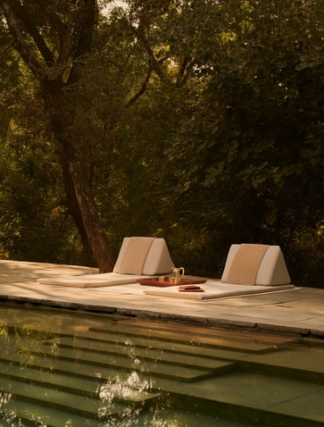 Two cushioned chairs on a wooden deck beside a still pool at Aman-i-Khas, framed by verdant trees.