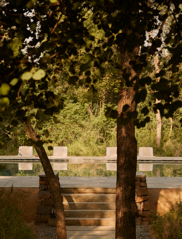 Two cushioned chairs on a wooden deck beside a still pool at Aman-i-Khas, framed by verdant trees.