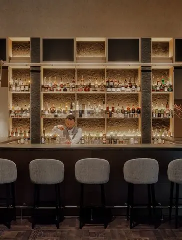 Bar della Rosa Alpina con ripiani illuminati di bevande e sgabelli neri al resort Aman Rosa Alpina.