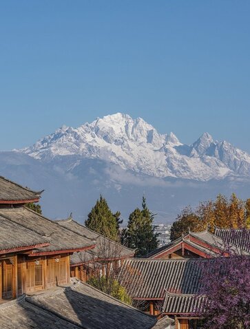 Snow-capped mountain rising behind traditional wooden buildings at Amandayan resort in spring.