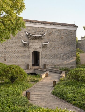Stone pavilion at Amanyangyun with traditional curved roof and timber pathway through manicured garden.