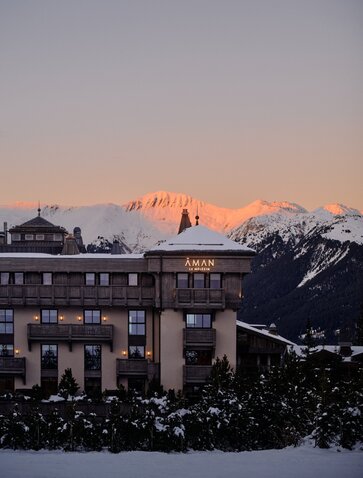 Aman Le Mélézin exterior at dusk with snow-covered peaks glowing in alpenglow light.