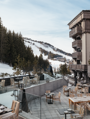 Terrace at Aman Le Mélézin with views towards snow-capped Alpine slopes and pine forest.