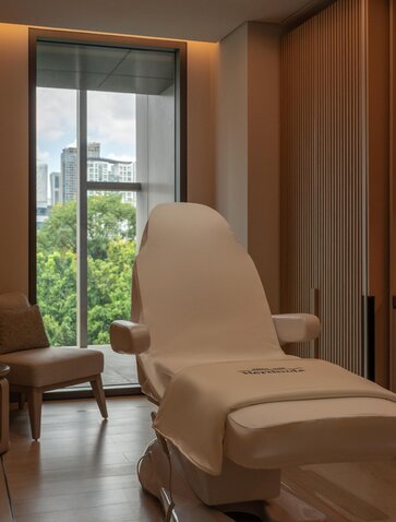 Wellness clinic treatment chair at Aman Nai Lert Bangkok, with garden views through floor-to-ceiling windows.