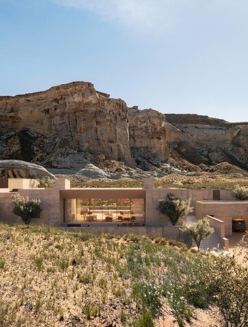 Amangiri resort residence with stone façade nestled against a desert hillside at sunset, surrounded by native vegetation.