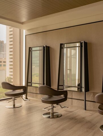 Spa treatment room at Aman Nai Lert Bangkok with mirrors, styling chairs and neutral tones.